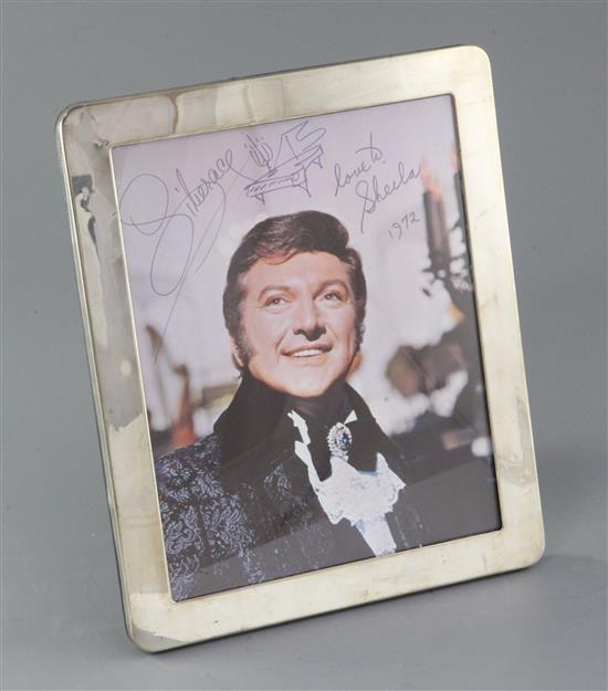 Liberace: An autographed colour photograph of Liberace, 10 x 8in., housed in a Theo Fennell silver photograph frame, overall 12 x 10in.